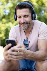 middle-aged man wearing headphones and using smartphone