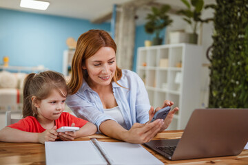 mother and daughter use mobile phone together in the living room