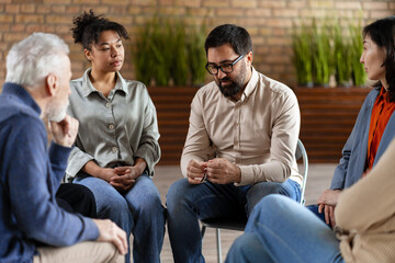 Diverse people sitting in circle supporting each other during group therapy session