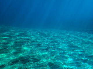 Obraz premium Ocean blue underwater with sunrays, Underwater Sea Deep Water Abstract Sunshine, sea wave , clean waters in summer time, Natural underwater seascape, sand on ocean floor and water surface with sunligh