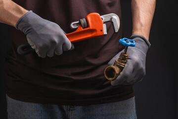 Plumber with pipe wrench and fitting on dark background, closeup.