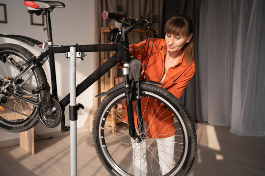 Active woman in orange shirt repairing and securing bicycle at home. cycling and biking leisure concept. DIY bike maintenance. - Powered by Adobe
