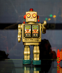 Retro tin robot toy with metallic body, colorful control panel details, and blue feet displayed upright on a reflective surface