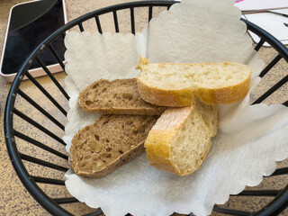 A black wire basket lined with white paper holds slices of brown walnut bread and white crusty...