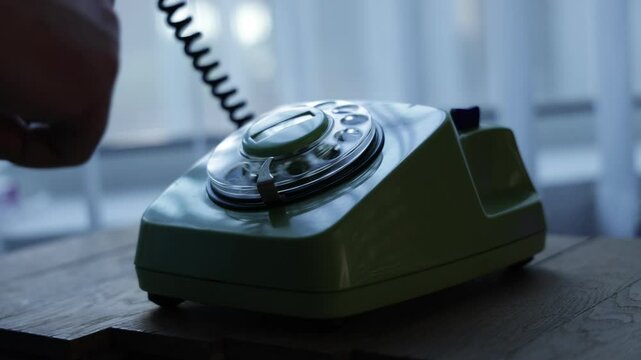 Close-up view of a hand picking up the telephone receiver and dialing numbers on an old rotary phone. Retro plastic phone.