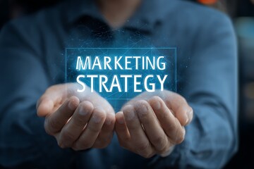 High quality photo of businessman holding a virtual marketing strategy icon and the text "MARKETING STRATEGY" in his hands. He is wearing a blue shirt against a dark background. The.