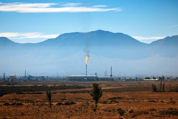 An industrial facility in Iran with a torch burning associated gases, Against the backdrop of mountains. Flares of Iranian oil refinery and smoking in the air, A factory hidden underground