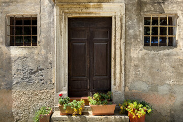 facade of old italian stone house with wooden door and lattice windows, flanked by potted plants on...