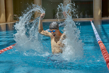 A competitive swimmer splashes water energetically in an indoor pool during a training session....