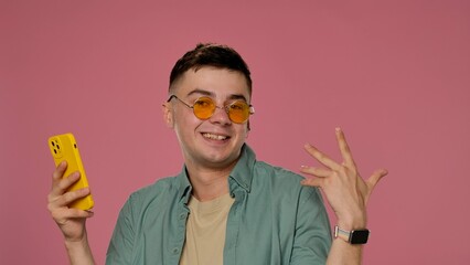 Cheerful Young Man with Smartphone and Sunglasses Against Pink Background