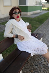 Elegant mature woman relaxing on bench in white dress