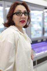 Woman wearing glasses and red lipstick looking down in supermarket refrigerator aisle