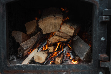 Close-up of burning firewood inside a black metal stove, with glowing embers and orange flames...