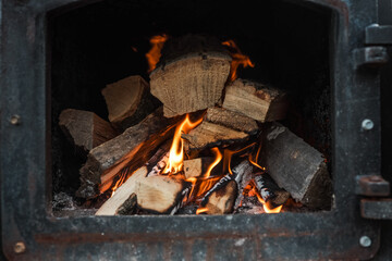 Close-up of burning firewood inside a black metal stove, with glowing embers and orange flames...