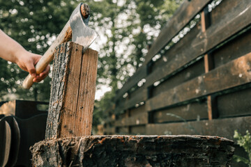 Close-up of a hand holding an axe embedded in a vertical log, ready for splitting firewood outdoors...