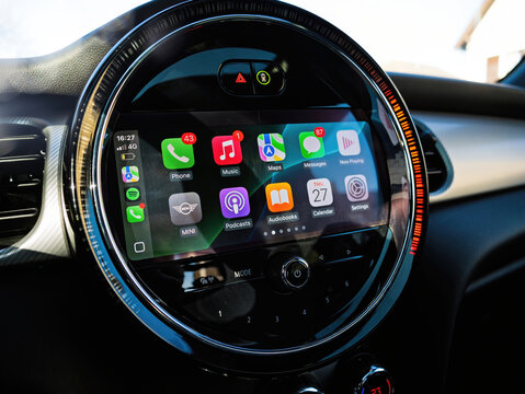 Paris, France - Mar 27, 2025: Close-up of a circular infotainment screen in a MINI electric car displaying Apple CarPlay interface with app icons like Music, Maps, and Messages in bright daylight