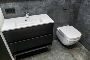 Stylish and functional bathroom interior featuring a sleek white sink with a black vanity, paired with a modern wall-mounted toilet, all set against dark gray tile walls
