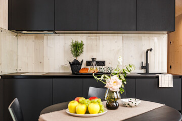 A cozy modern kitchen featuring a table with fresh fruits, a pink rose in a vase, and a dotted...
