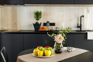 A cozy modern kitchen featuring a table with fresh fruits, a pink rose in a vase, and a dotted...
