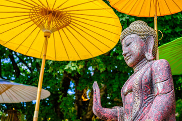 Serene Buddha statue under colorful parasols in a tranquil garden setting during a sunny afternoon