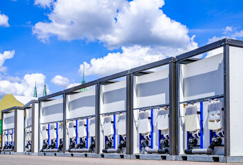 Portable restroom facilities lined up in a construction area under a blue sky with scattered clouds during daytime hours