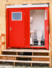 Portable restroom facilities lined up in a construction area under a blue sky with scattered clouds during daytime hours