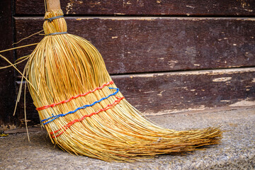 Traditional straw broom rests against a wooden shelf in a rustic setting during afternoon light