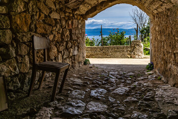 Passage under the walls of the old town in Vrbnik, an old wooden chair, a resting place for tourists KRK Croatia