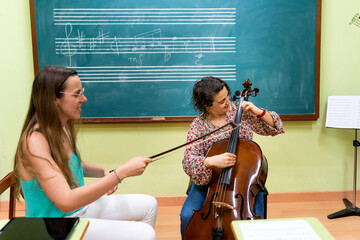 Music teacher helping student playing cello in a classroom