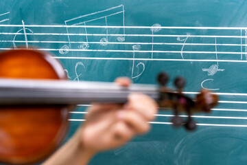 Musician playing violin during music lesson in front of blackboard with musical notes