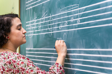 Music teacher writing musical notes on blackboard in classroom