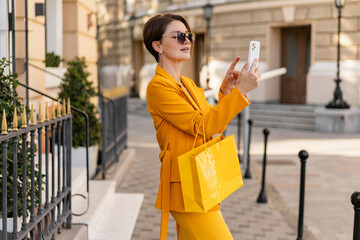 stylish elegant woman on shopping in city street wearing bright colorful yellow suit summer style