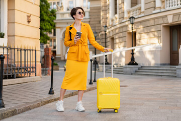 stylish woman traveling with yellow suitcase in Europe