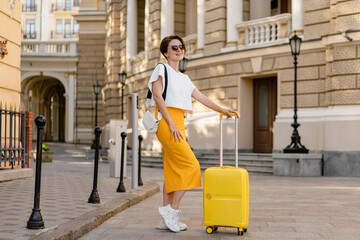 stylish woman traveling with yellow suitcase in Europe