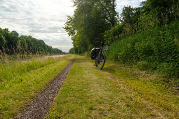 Fahrrad mit Gepäcktaschen an idyllischem Kanalradweg im Grünen. Sommerliche Landschaft, Natur pur und perfekte Kulisse für Outdoor-Abenteuer und Radreisen.