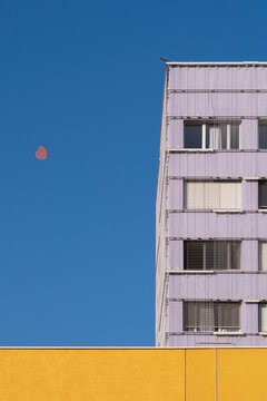 Yellow and white building detail with visible moon in Montpellier, France, showing playful urban contrast and clear geometric rhythm in strong daylight