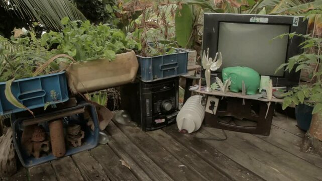 Wide shot of decorative waste with broken tv, stereo and plants at a Darien Gap rustic house in Colombia.