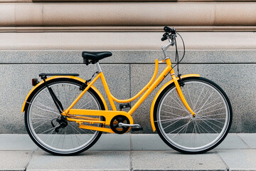 Bright yellow bicycle parked against a textured wall in the city