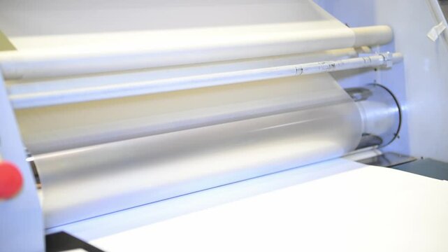 An industrial laminator with rotating shafts laminates, applies a transparent film to paper in the production room of the printing house
