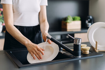 Modern kitchen sink with a person handwashing dishes on a black countertop