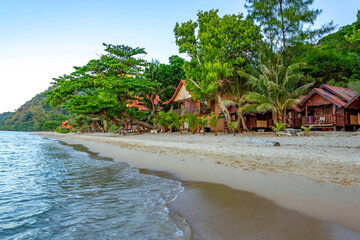 White Sand Beach at dawn: calm sea meets wet and dry sand, palm trees framing empty bungalows in morning shadows. Koh Chang, Thailand.

