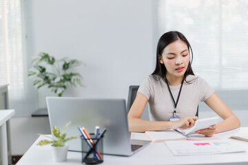Young focused asian businesswoman wearing headset using calculator and working with laptop computer at modern office, business and finance concept
