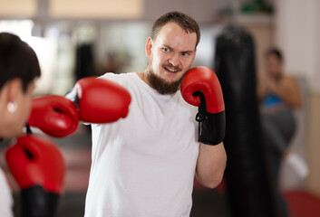 During training, bearded man wearing boxing gloves learns how to fight opponent. He punches, tries...