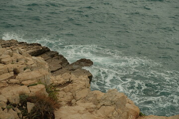 Jagged limestone rocks meet the rough Adriatic Sea as waves crash into the rugged shoreline. The dynamic contrast of textured stone.