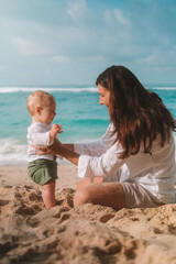 Portrait of mother and baby on vacation on the beach by the ocean. The little boy is capricious and...