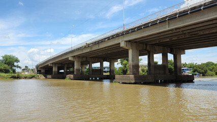 Concrete bridge over river with clear blue sky background, daytime scene of infrastructure and civil engineering, perspective from below showing water and structural details, transportation and develo