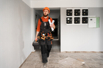 Builder repairman laborer wearing orange helmet in corridor with toolbox and tool belt