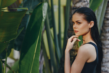 Exotic Asian woman with long black hair posing near lush green plants and palm trees