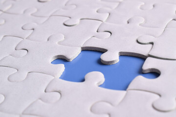 White puzzle with missing piece on blue background, closeup