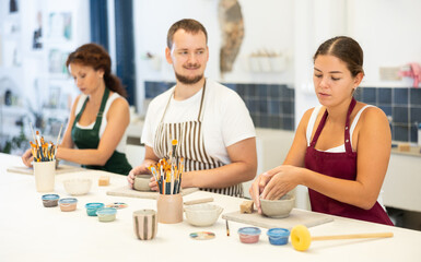 During working day, three pottery workshop workers sculpt from raw clay. They smooth surface of...